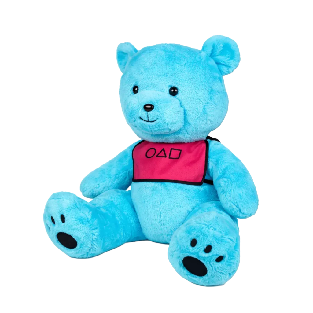 Blue teddy bear plush toy sitting upright wearing a pink bib with geometric symbols on a white background.