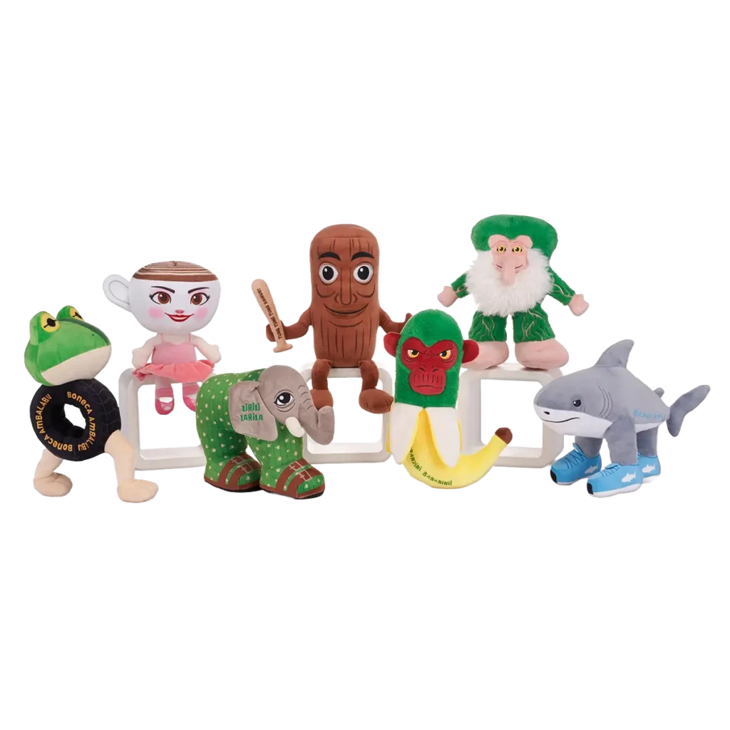 Collection of assorted character plush toys including frog with tire, ballerina teacup, wooden log mascot, elephant, banana monkey, green troll and shark with sneakers.